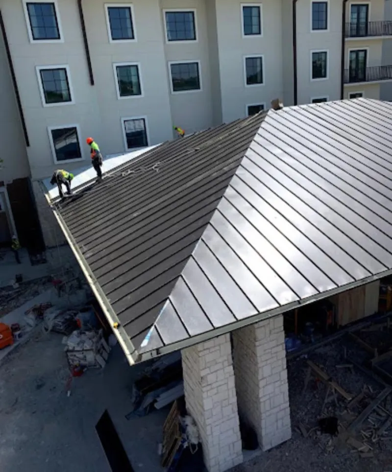 Crew installing standing seam metal roof panels on a commercial project in Oneonta